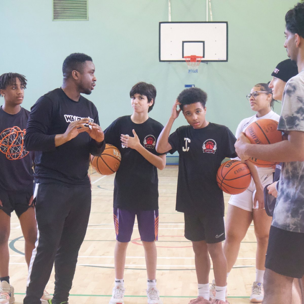 Coach talking to young players holding basketballs